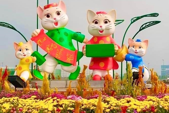 Linh vật của năm là gia đình mèo tay cầm câu đối, thỏi vàng, bánh chưng, bánh tét, nhành mai, biểu trưng đón chào năm mới an lành, thịnh vượng, tràn đây năng lượng.
