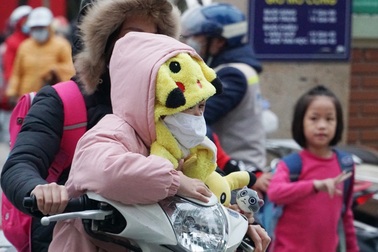 Trẻ em được bố mẹ bọc kín mít đi đường trong tiết trời lạnh giá ở Hà Nội