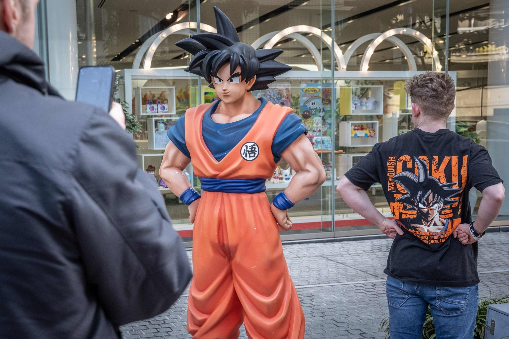 Du khách mặc áo phông hình "Dragon Ball" chụp ảnh với bức tượng Son Goku ở Tokyo (Ảnh: AFP).