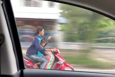 Người phụ nữ chở con nhỏ bằng xe máy thả cả 2 tay để dùng điện thoại