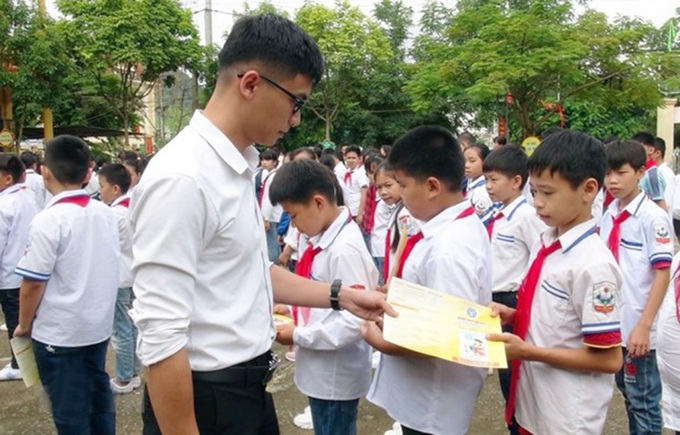 Cán bộ bảo hiểm phát tờ rơi tuyên truyền về bảo hiểm y tế học sinh. (Ảnh: Hữu Quyết/TTXVN)