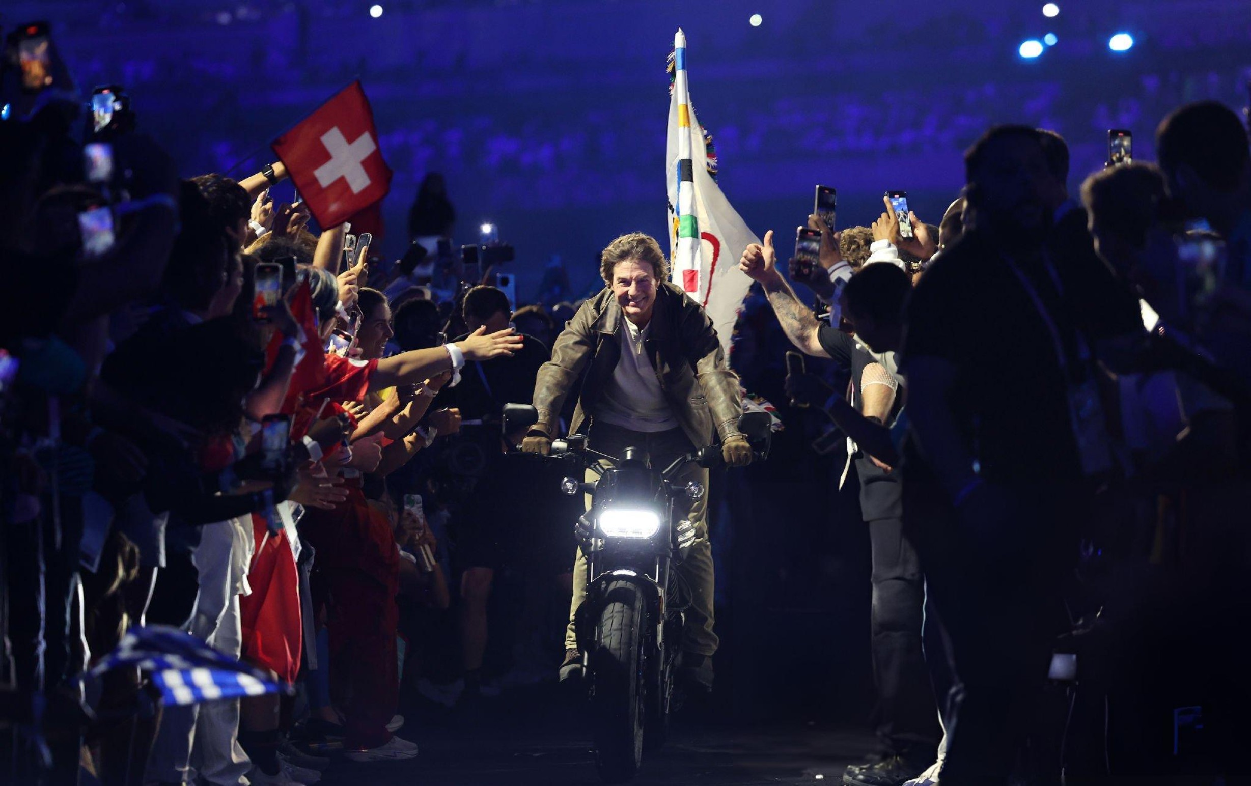 Tom Cruise cưỡi mô tô mang theo lá cờ Olympic.