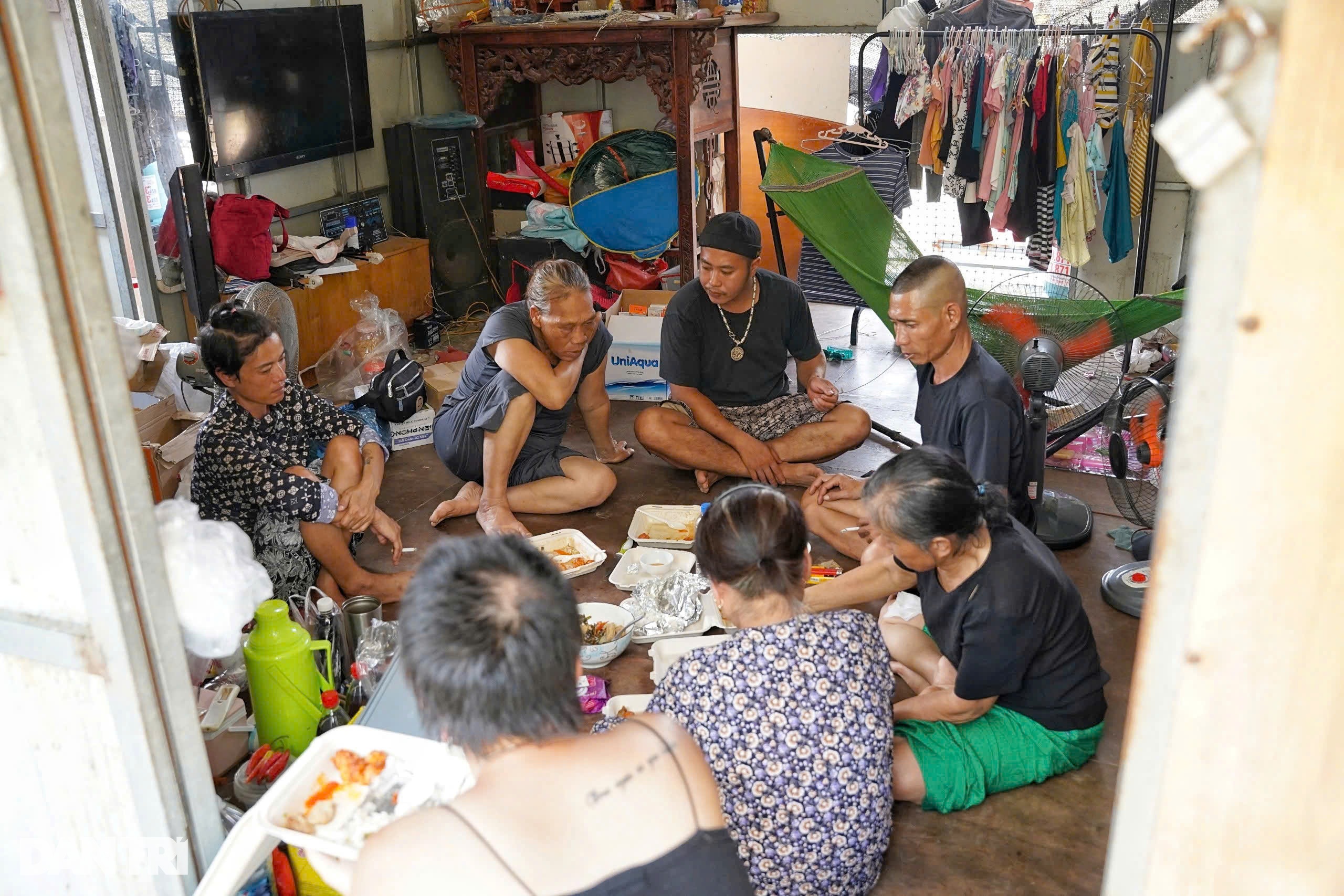 Vợ chồng Hiền tá túc trong căn nhà phao của hàng xóm, ăn cơm hộp do nhóm thiện nguyện gửi tặng (Tuấn đội mũ, đeo dây chuyền) (Ảnh: Ngọc Tân).