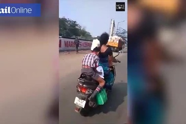 Cậu bé Ấn Độ vừa ngồi sau xe mẹ vừa thoăn thoắt làm bài tập về nhà