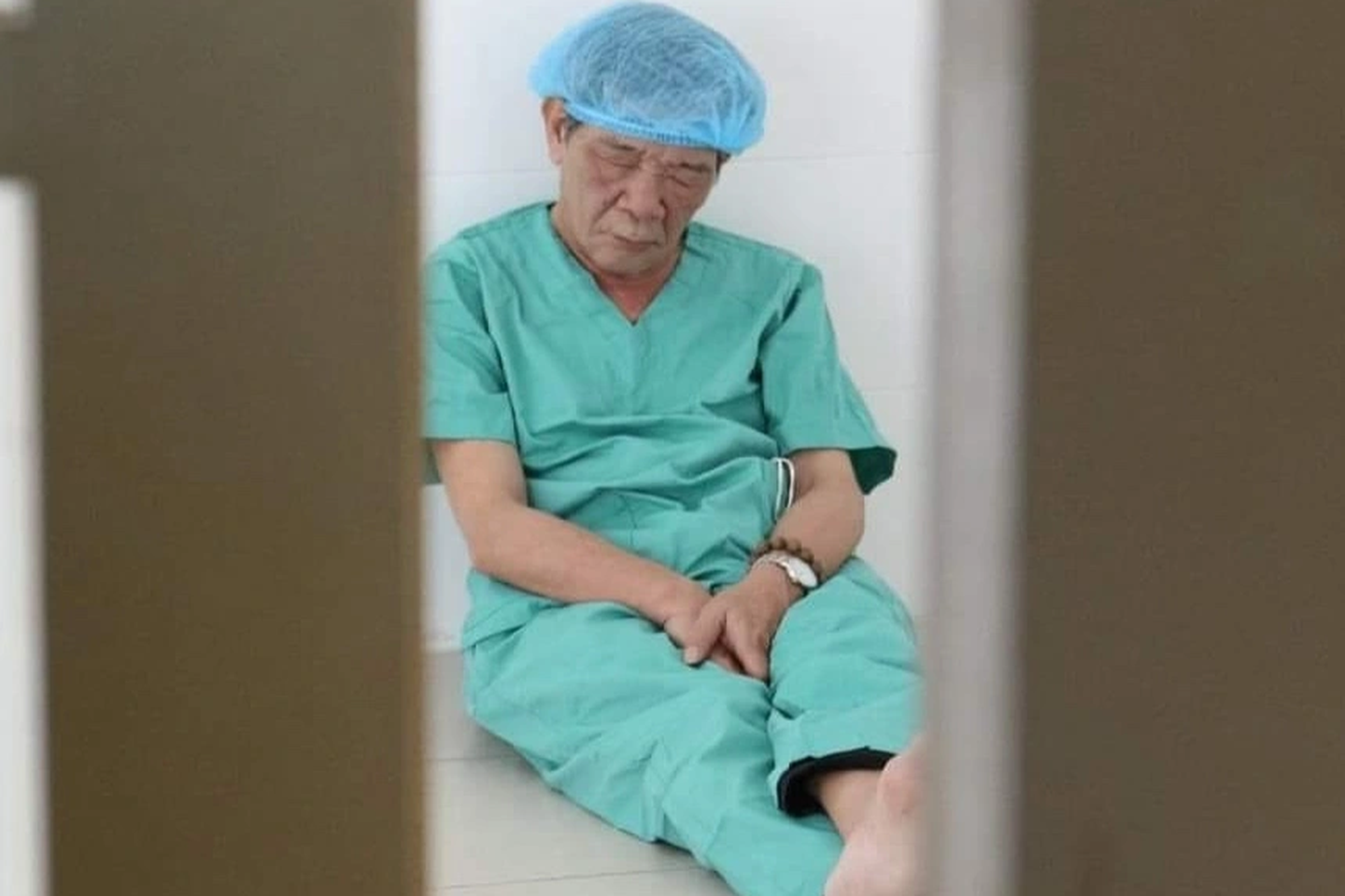 Bác sĩ ngồi trên sàn nhà, lưng dựa tường chợp mắt sau phẫu thuật từ thiện