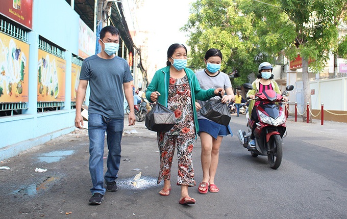 8h sáng, bà Sương (giữa) cùng cháu gái mua được 2 suất khẩu trang và ra về. Bà nói: Người nào có số mới được vào trong mua, phải chuẩn bị sẵn tiền lẻ, khẩu trang và nước rửa tay đã được nhân viên để sẵn trong túi ni lông. Ảnh: Diệp Phan.