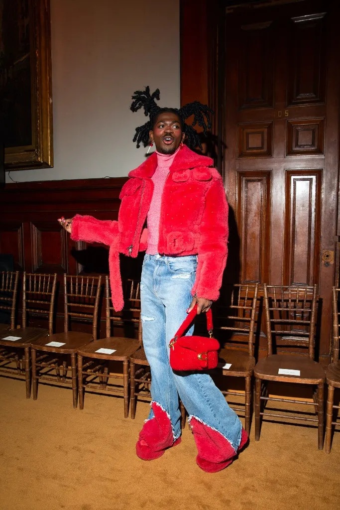 Ca sĩ Lil Nas X mang đến sắc màu rực rỡ hơn khi diện áo khoác lông xù đỏ, xếp lớp trên chiếc áo cổ lọ màu hồng lấp lánh. Bộ trang phục được hoàn thiện với quần jeans xanh có viền đỏ và túi xách Tabby (Ảnh: Lexie Moreland).