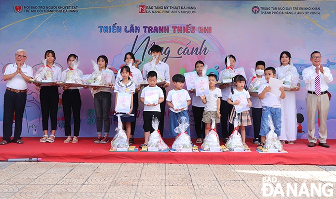 Nguyên Phó Chủ tịch UBND thành phố Đà Nẵng, Chủ tịch Hội Bảo trợ người khuyết tật và trẻ mồ côi Nguyễn Hoàng Long (bìa trái) và Giám đốc Bảo tàng Mỹ thuật Đà Nẵng Hà Thanh Vân (bìa phải) tặng quà và giấy chứng nhận tham gia triển lãm cho các em thiếu nhi. Ảnh: baodanang.vn