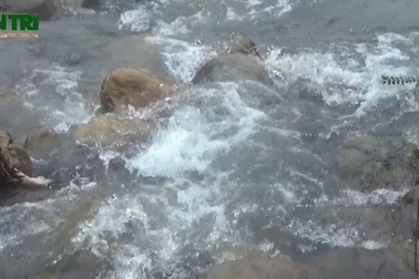 Hai người đàn ông cõng học sinh đi trên ống nước bắc qua con suối dữ